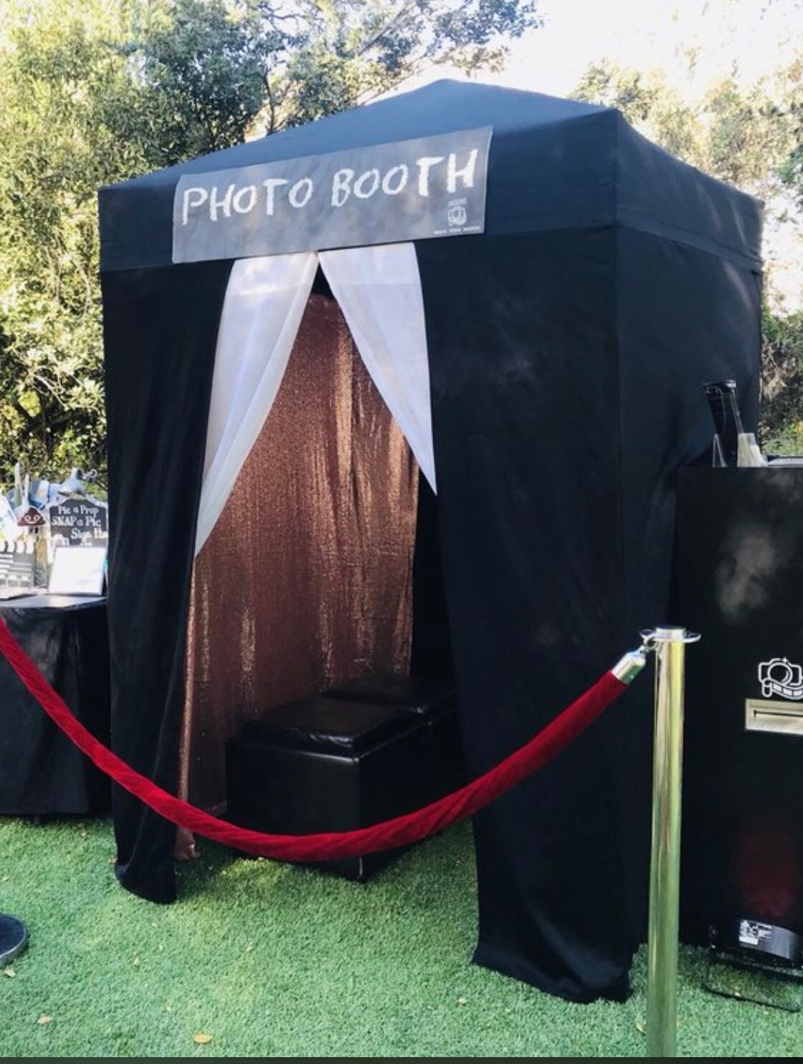 Photo booth with black tent, red velvet rope, and a metallic backdrop.