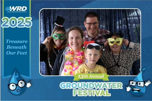 People posing in a photo booth at the Groundwater Festival. They wear masks and props in front of a blue backdrop.