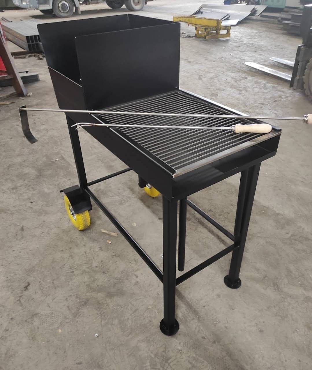 Griglia in metallo nero su ruote con griglia, focolare e lungo attizzatoio, posizionata all'interno.