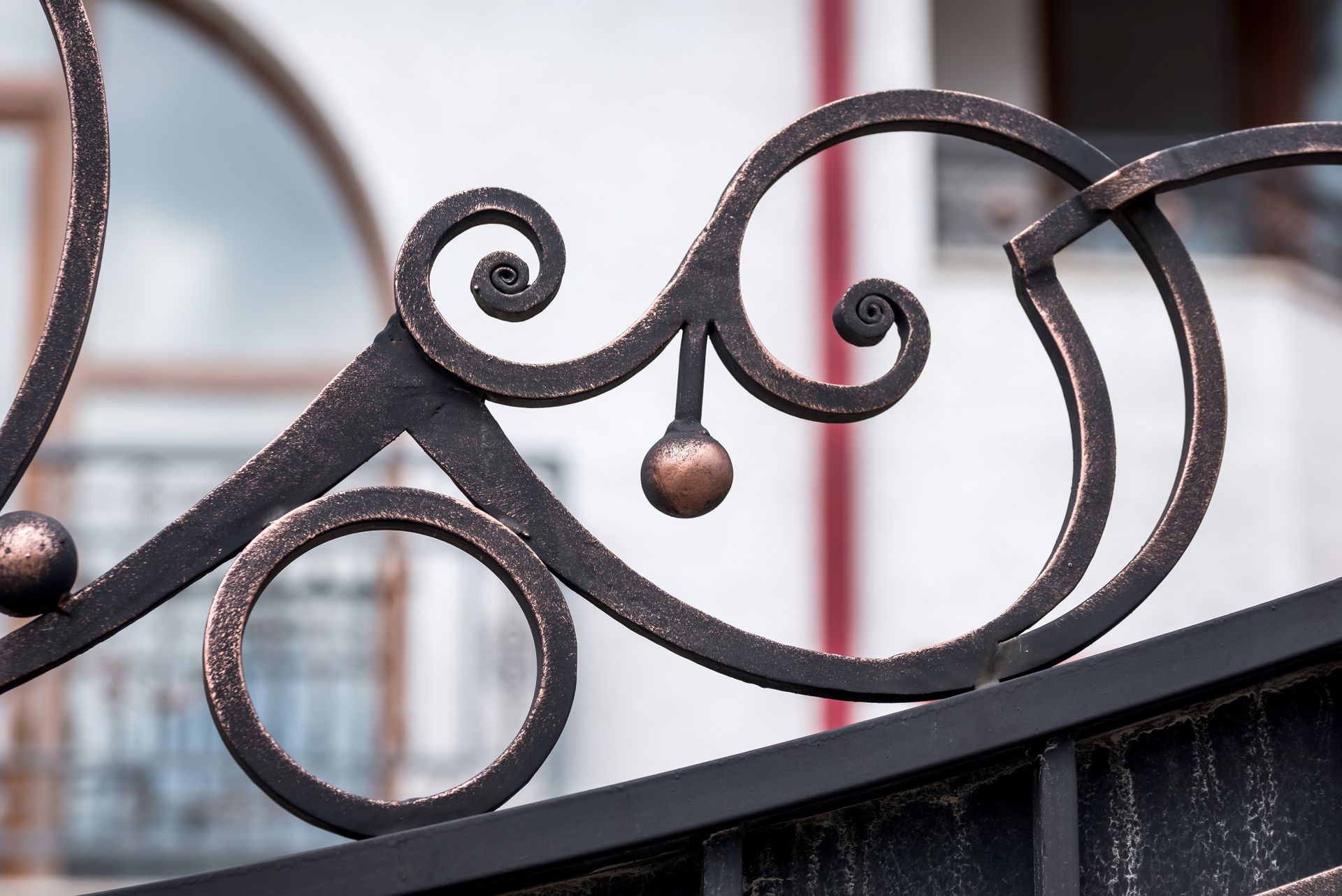 Dettaglio di un cancello in ferro battuto decorato con vortici, cerchi e una sfera centrale in bronzo.