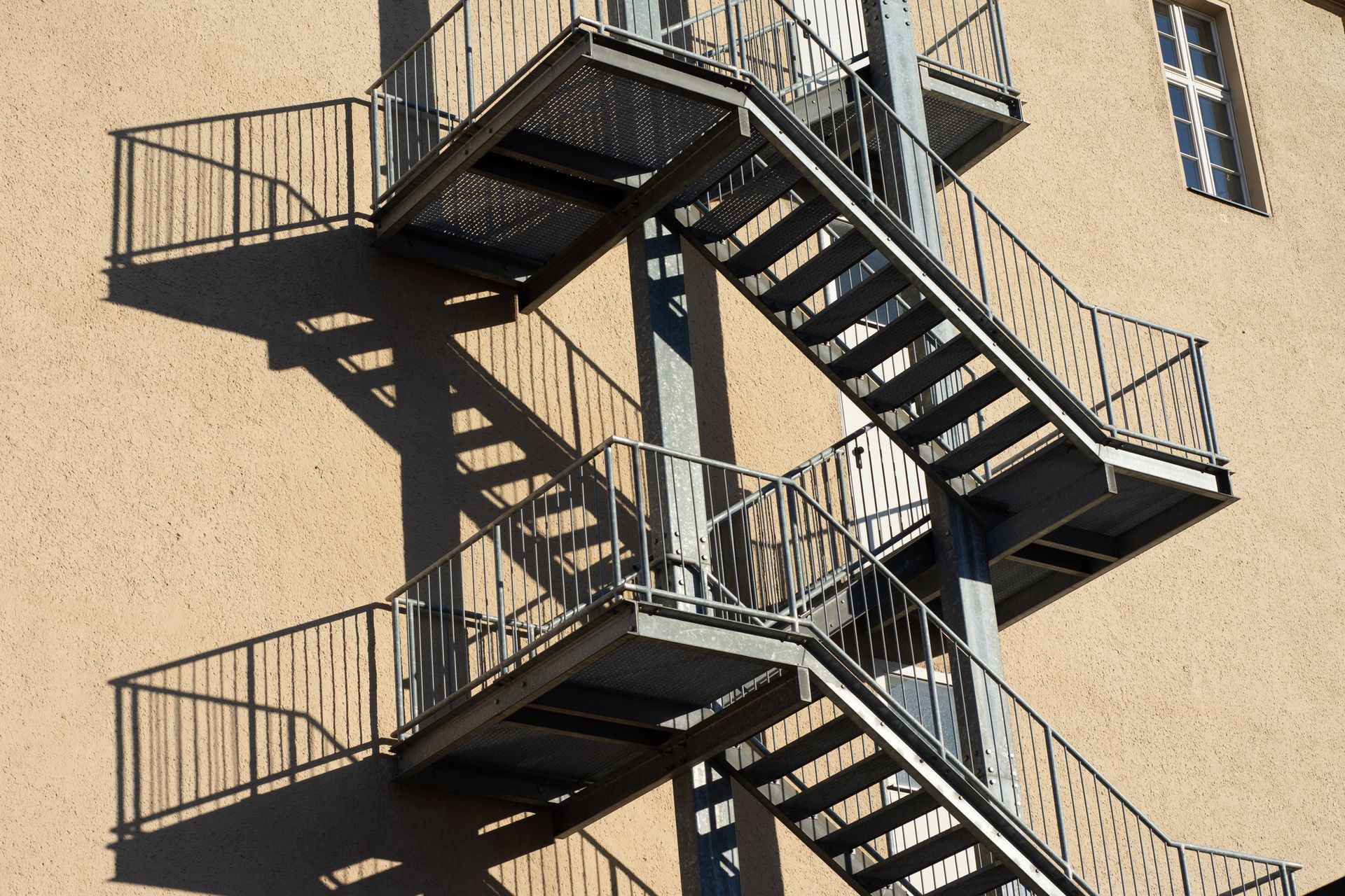 Scala antincendio in metallo fissata all'esterno di un edificio color marrone chiaro con finestra.