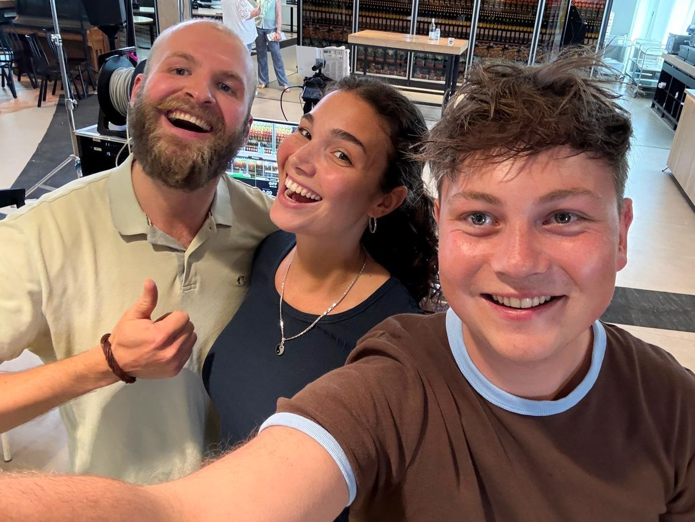 Drie mensen lachend voor een selfie; twee mannen en een vrouw binnen.