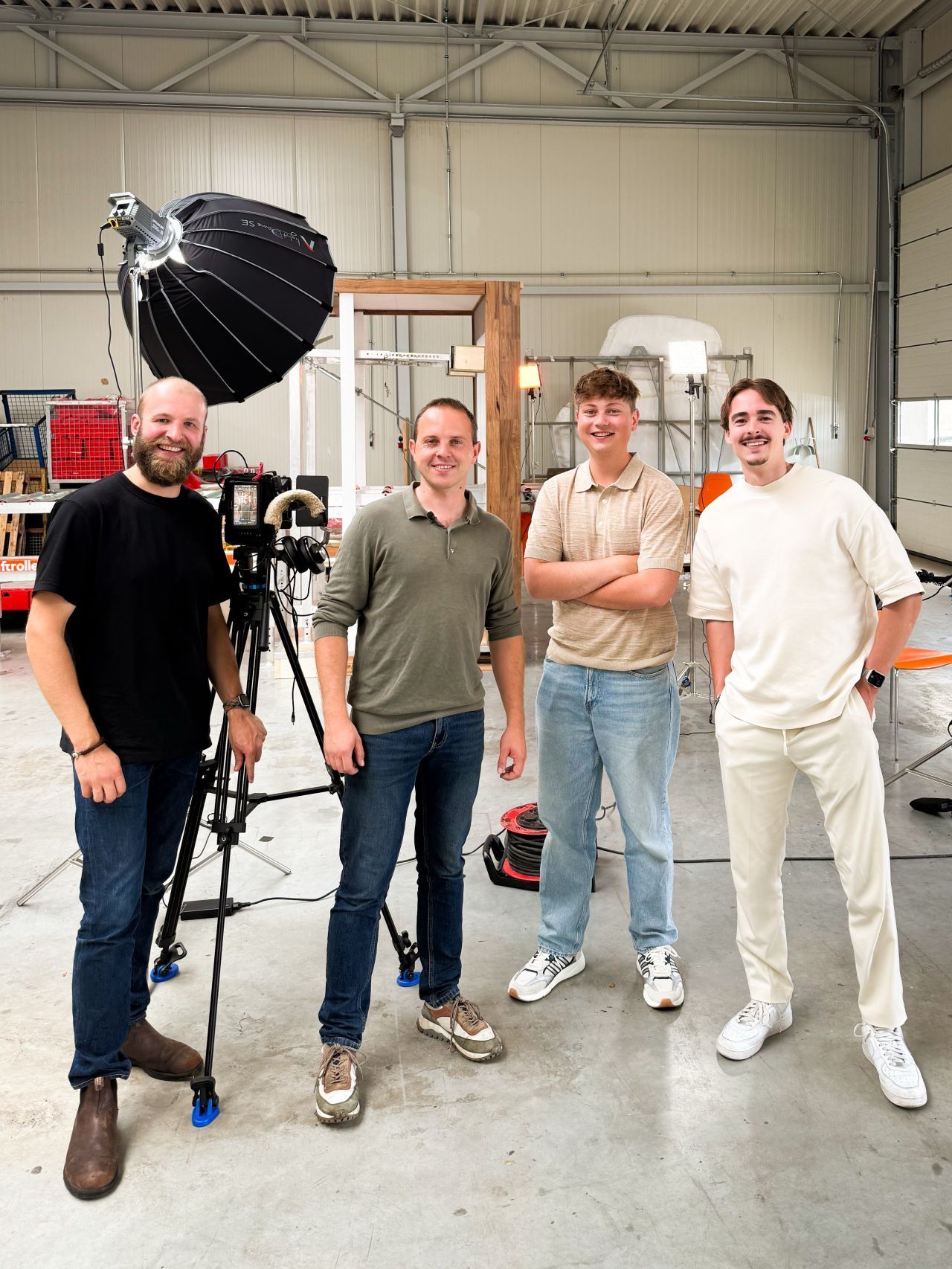 Vier mensen staan ​​in een studio met camera-apparatuur. Eén man bedient de camera. De anderen glimlachen.