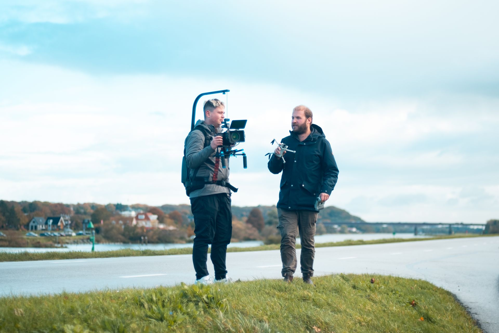 Twee mannen filmen in de buitenlucht: de ene met een camera-installatie en de andere met een kleine camera.