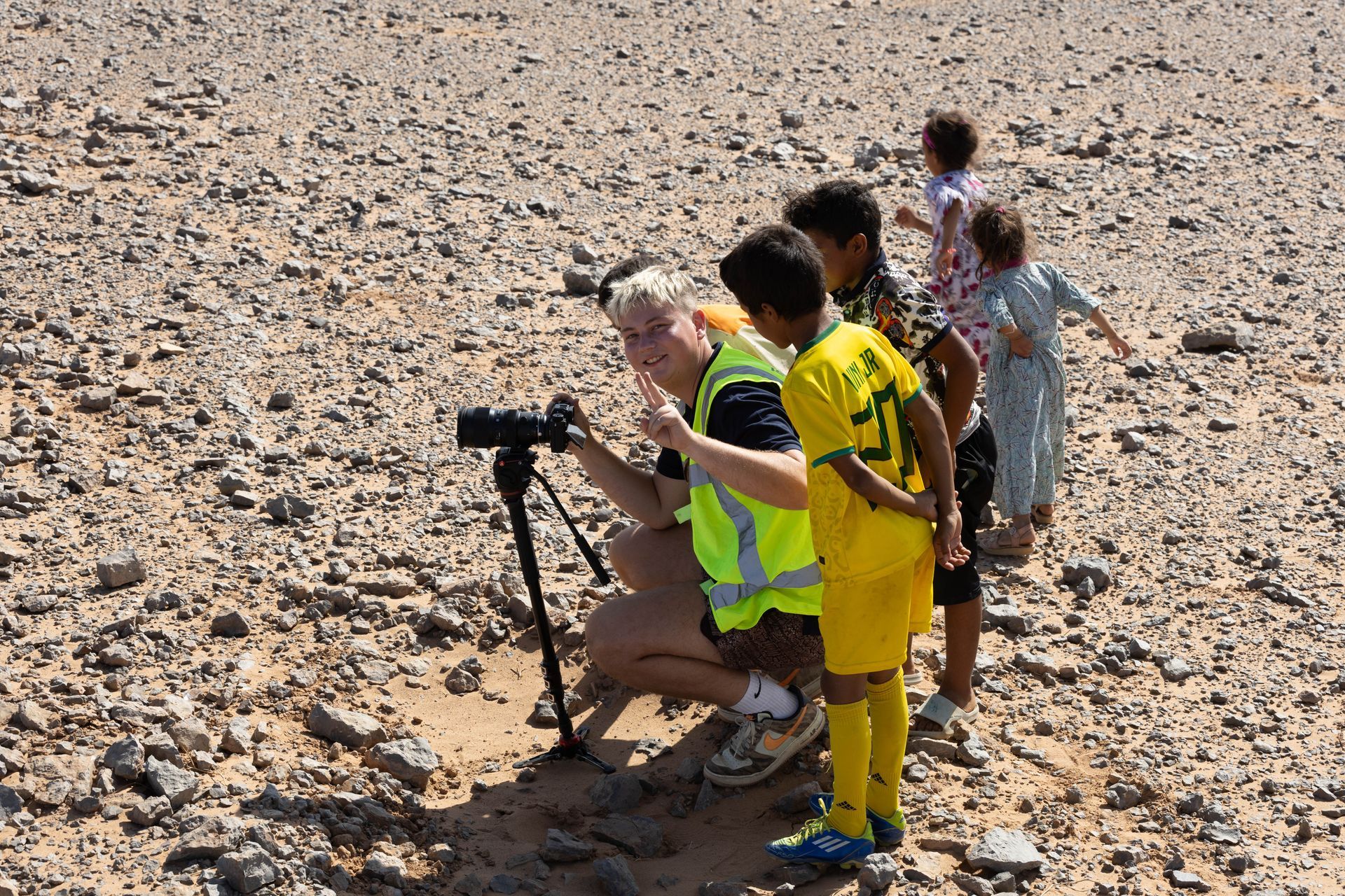 Een fotograaf knielt op een rotsachtige ondergrond en maakt foto's van kinderen in felgekleurde kleding.