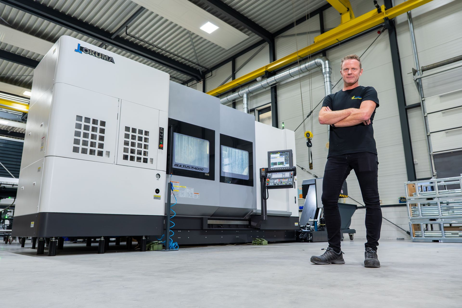 Een man staat met gekruiste armen voor een grote industriële machine in een fabriek.