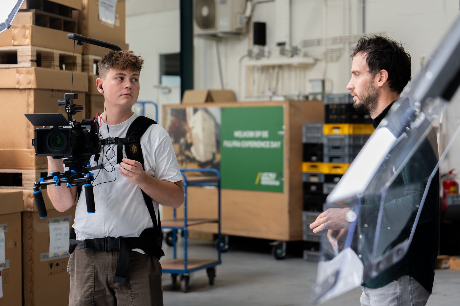 Iemand filmt met een camera een andere persoon in een magazijnomgeving.