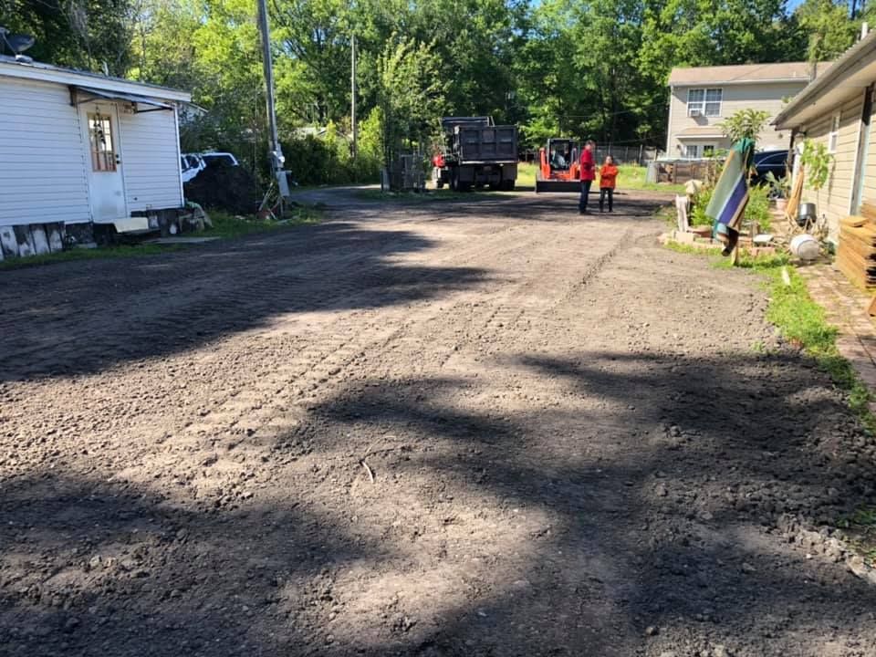 Dirt driveway with two people in safety vests, a small truck, and houses.