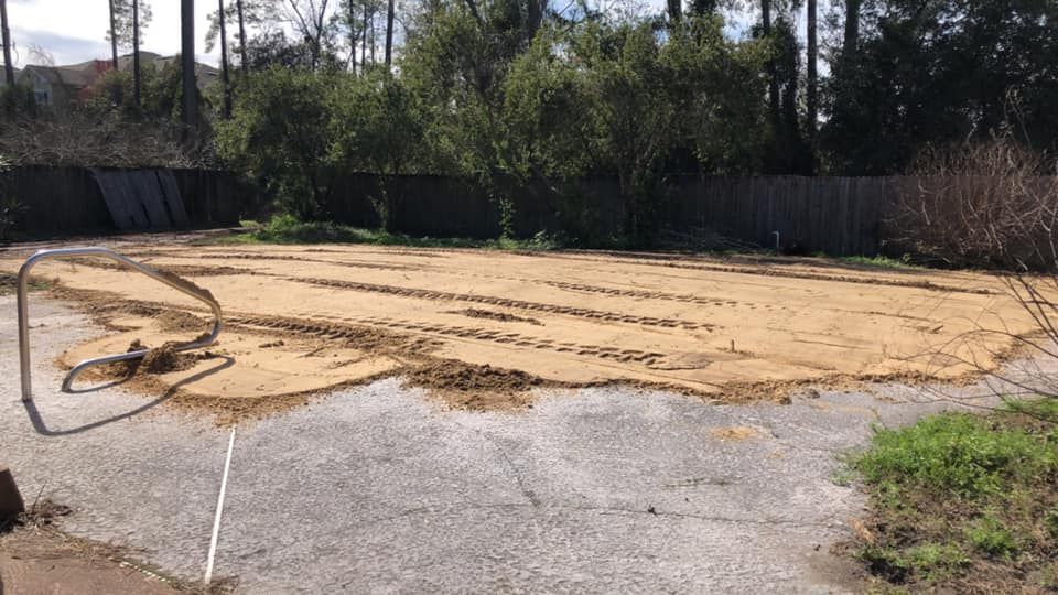 A concrete backyard area covered with sand, tracks, and a partially disassembled basketball hoop.