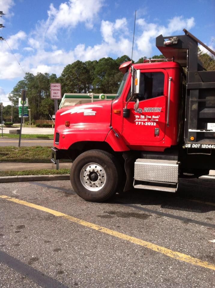 Red dump truck parked next to a curb in front of a green sign under a cloudy sky.