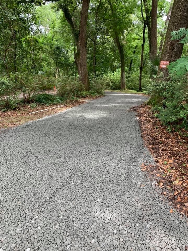 Gravel path curves through a shaded forest, surrounded by trees and greenery.