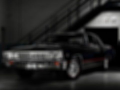 Black classic car with red stripe, parked under stairs.