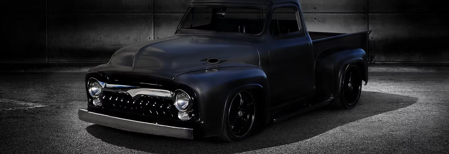 Black vintage pickup truck parked on a dark, textured surface with dramatic lighting.