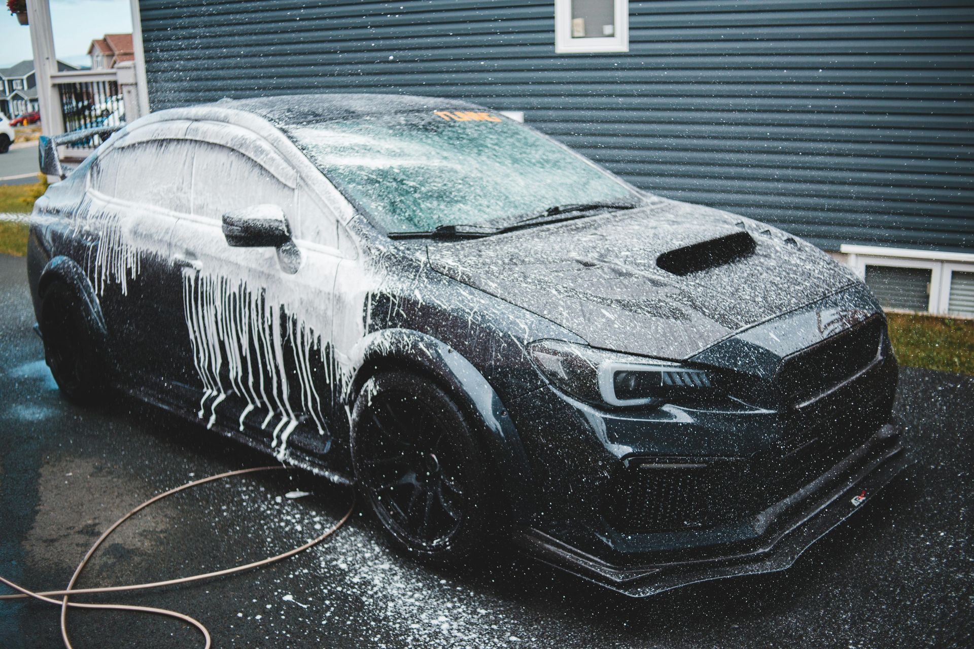 Black car covered in white foam being washed outside.