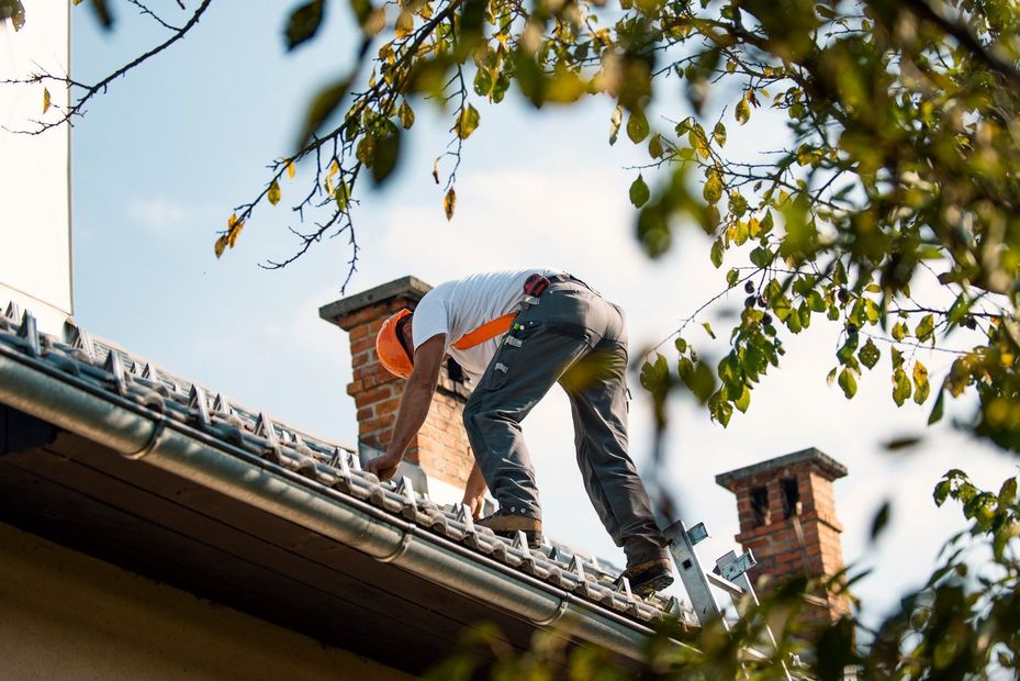 Operai al lavoro sul tetto in tegole di terracotta di una casa chiara in una giornata di sole. Due operai si avvicinano alla casa.