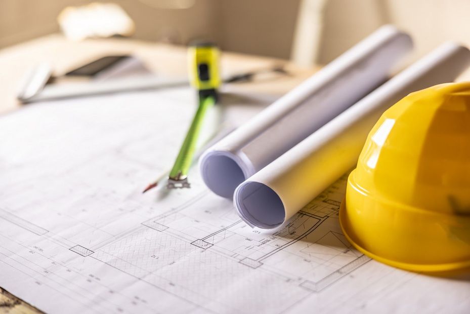 Un operaio edile esamina un muro di mattoni, indossando un casco e un giubbotto di sicurezza.