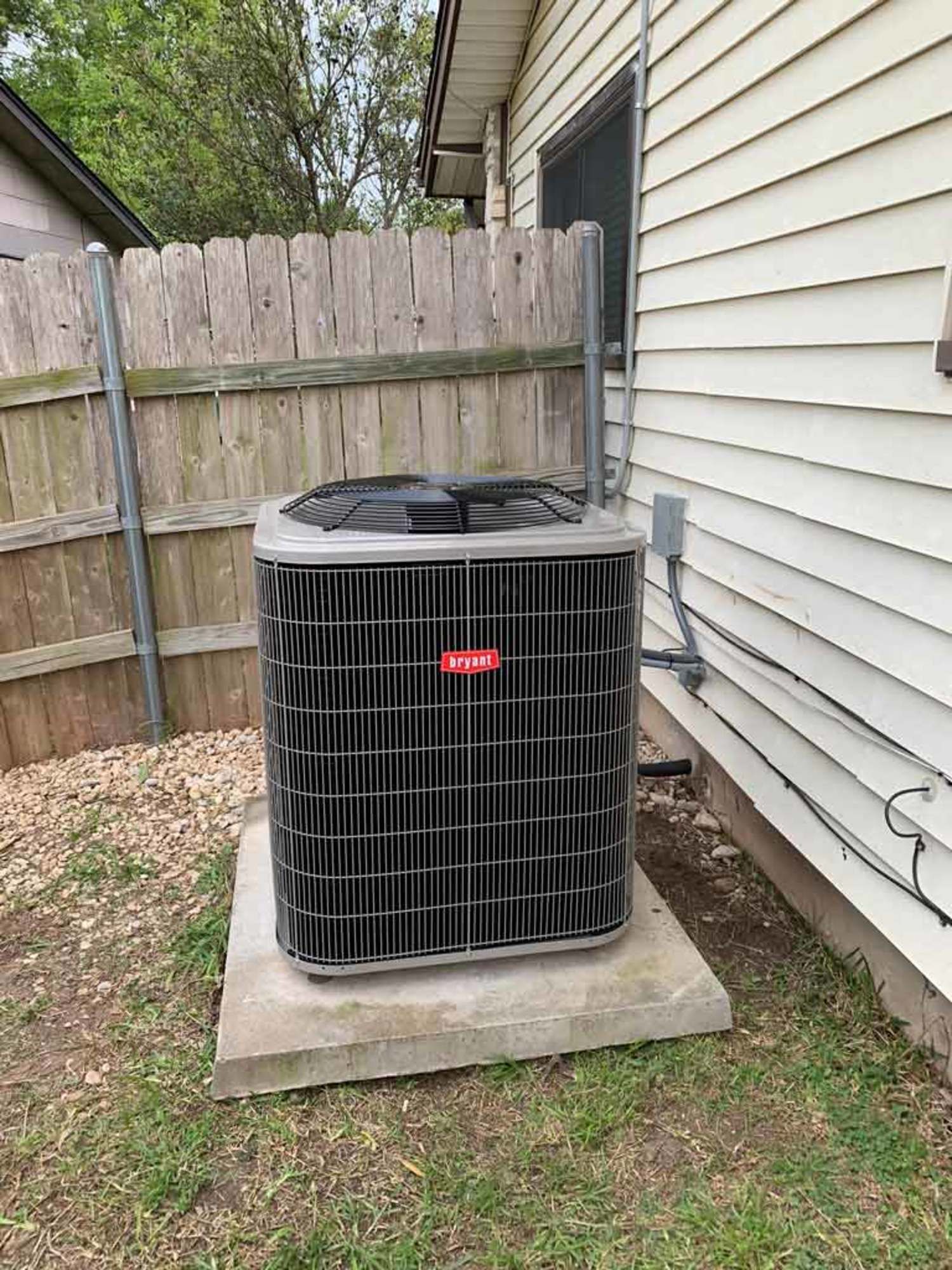 an air conditioner is sitting on the side of a house next to a wooden fence .