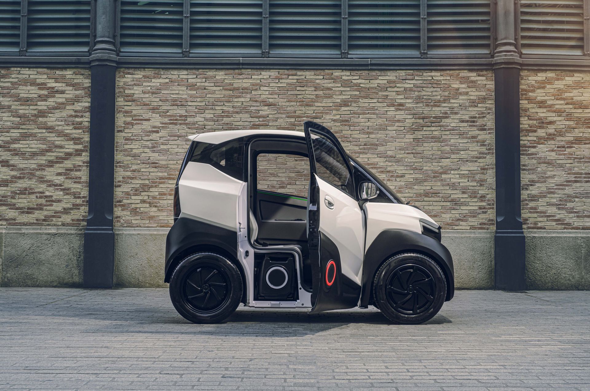 Una piccola automobile elettrica bianca è parcheggiata davanti a un muro di mattoni.