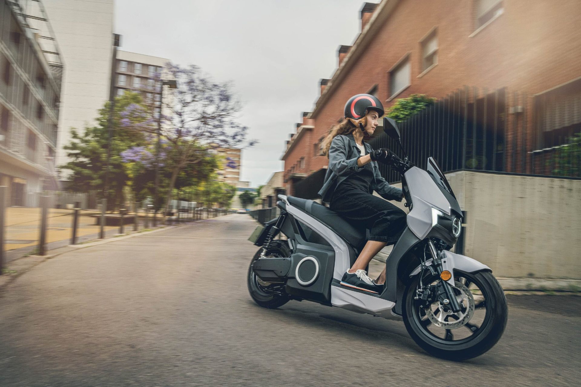 Una donna sta guidando uno scooter lungo una strada cittadina.