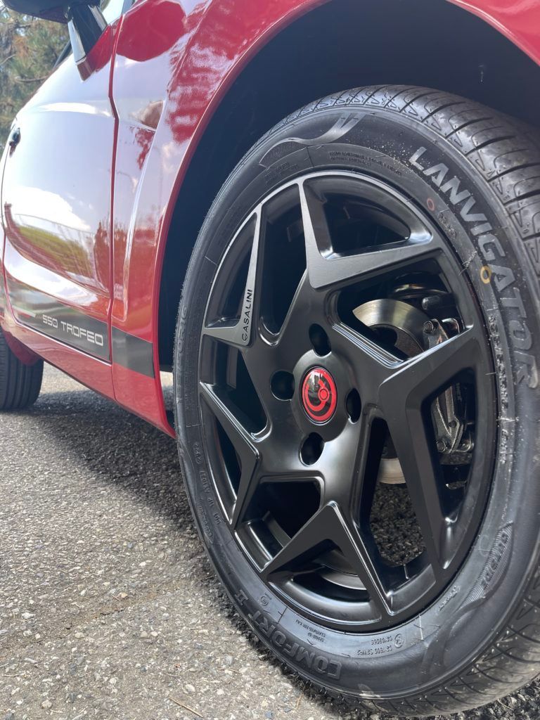 Un'auto rossa con ruote e pneumatici neri è parcheggiata sul ciglio della strada.