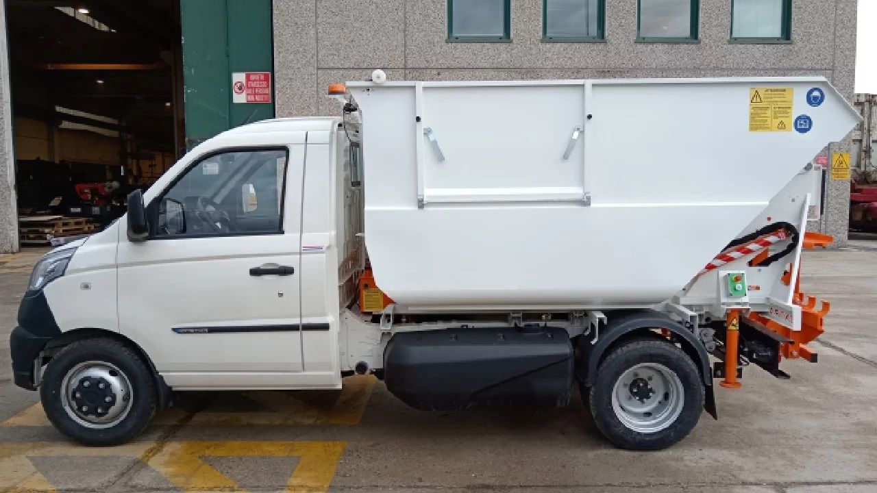 Un camion della spazzatura bianco è parcheggiato davanti a un edificio.