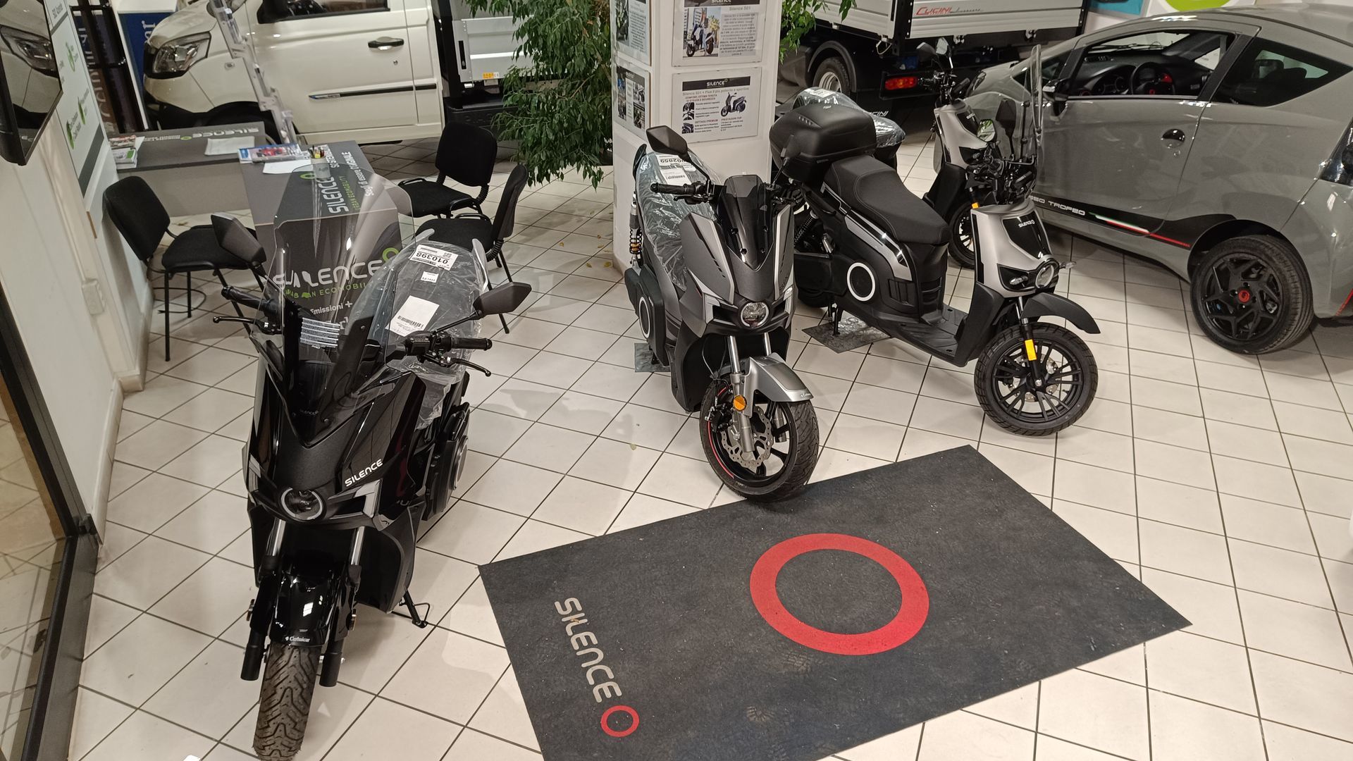Tre motociclette sono parcheggiate in uno showroom accanto a un'auto.