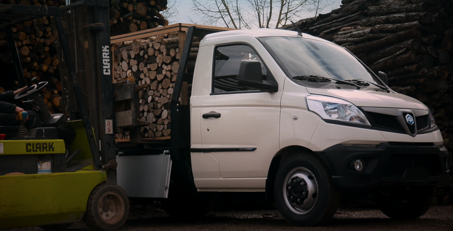 Un furgone bianco viene caricato con dei tronchi tramite un carrello elevatore.