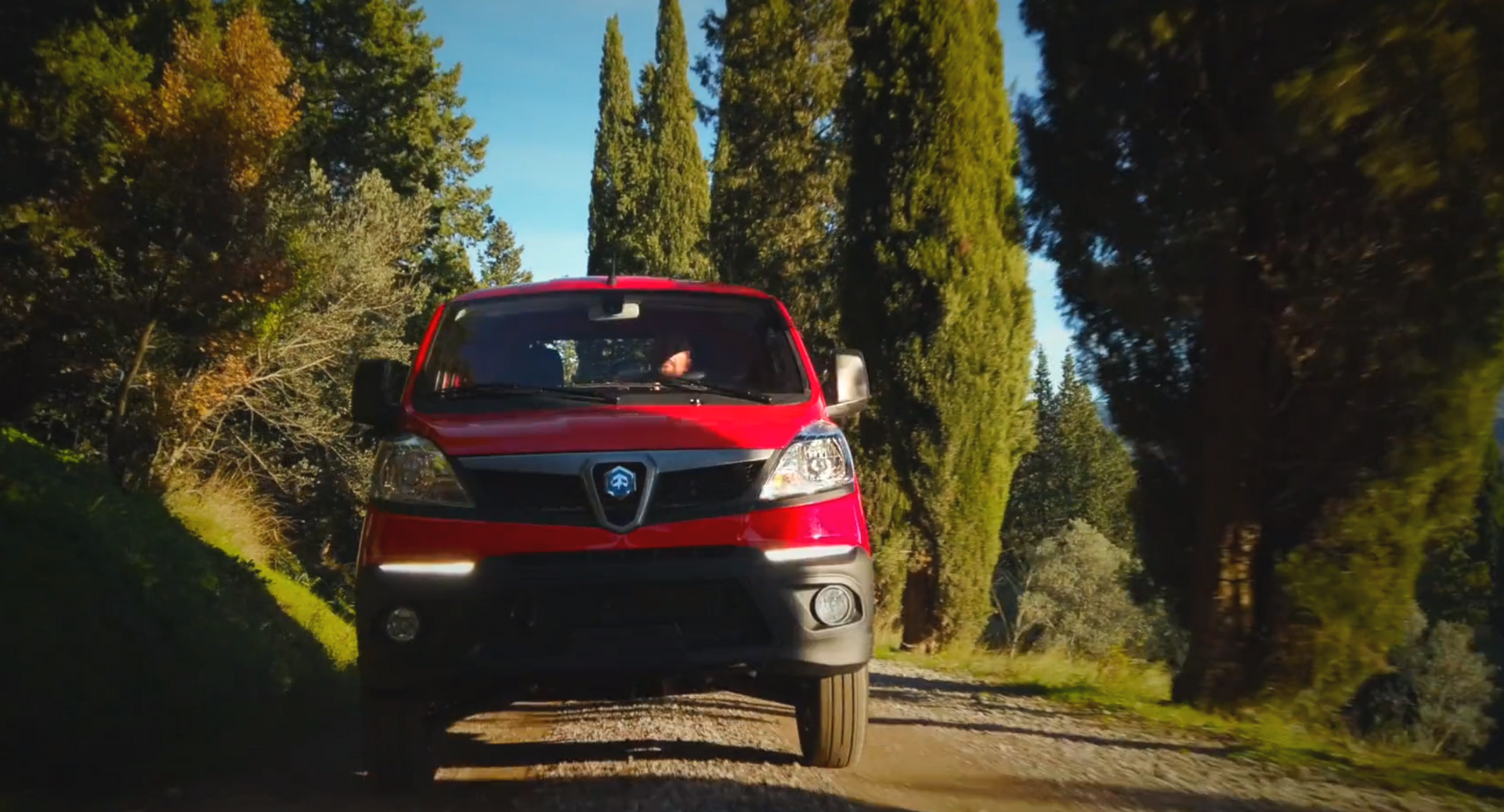 Un camion rosso sta percorrendo una strada sterrata circondata da alberi.