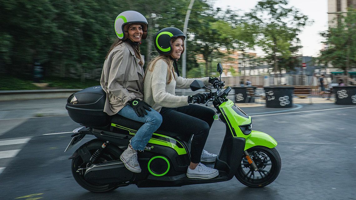 Due persone stanno guidando uno scooter verde lungo una strada.