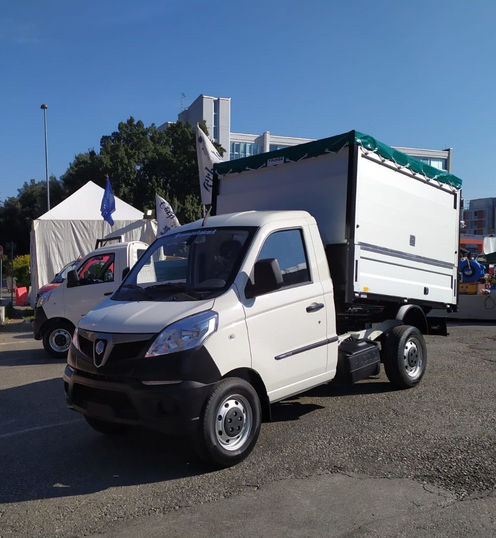 Un camion bianco con un telo verde sul retro è parcheggiato in un parcheggio.