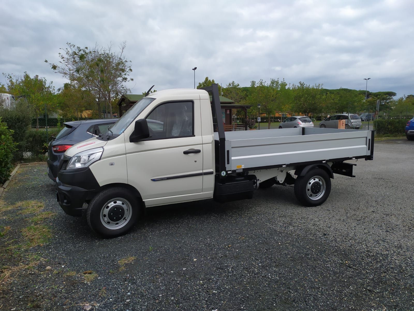 Un camion bianco con cassone è parcheggiato in uno spiazzo ghiaioso.