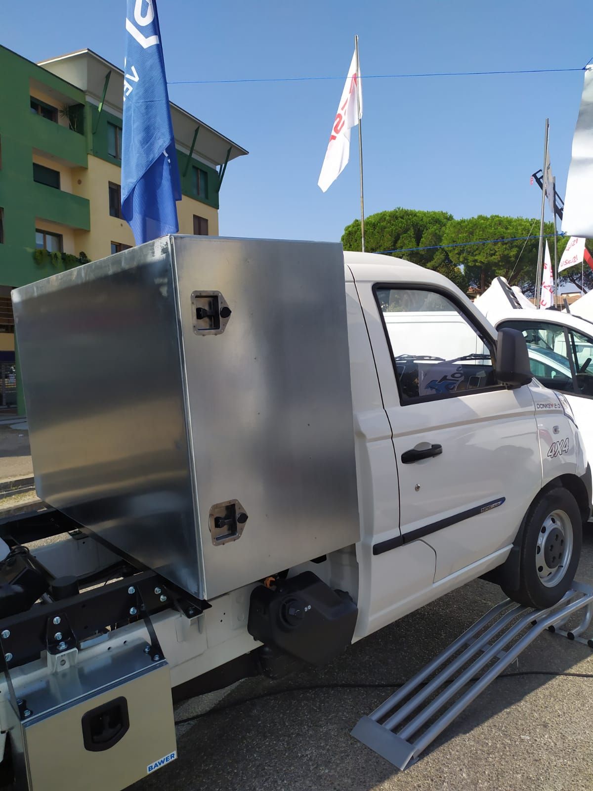 Un camion bianco con un cassone in acciaio inossidabile sul retro è parcheggiato sul ciglio della strada.