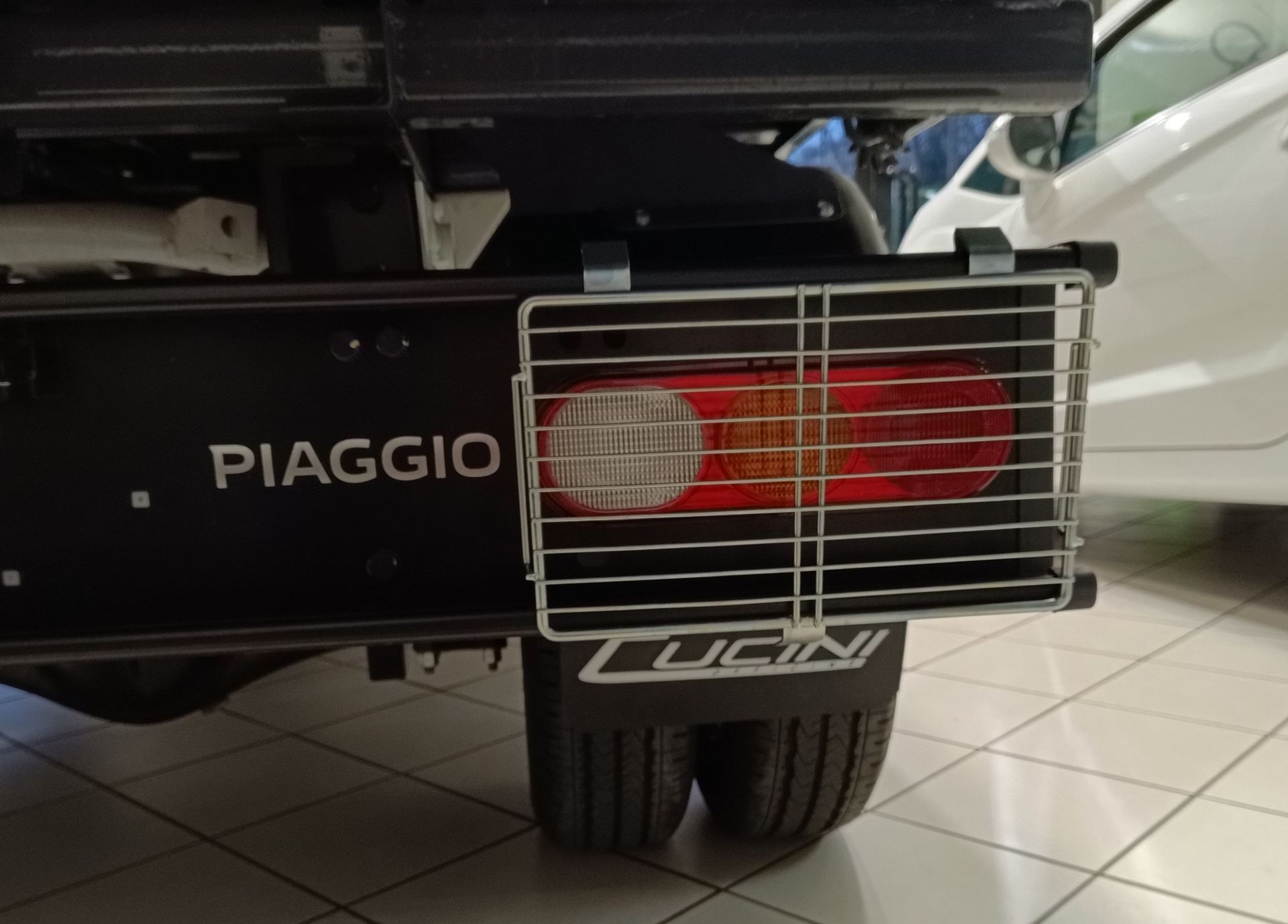 Un camioncino Piaggio nero è parcheggiato accanto a un'auto bianca