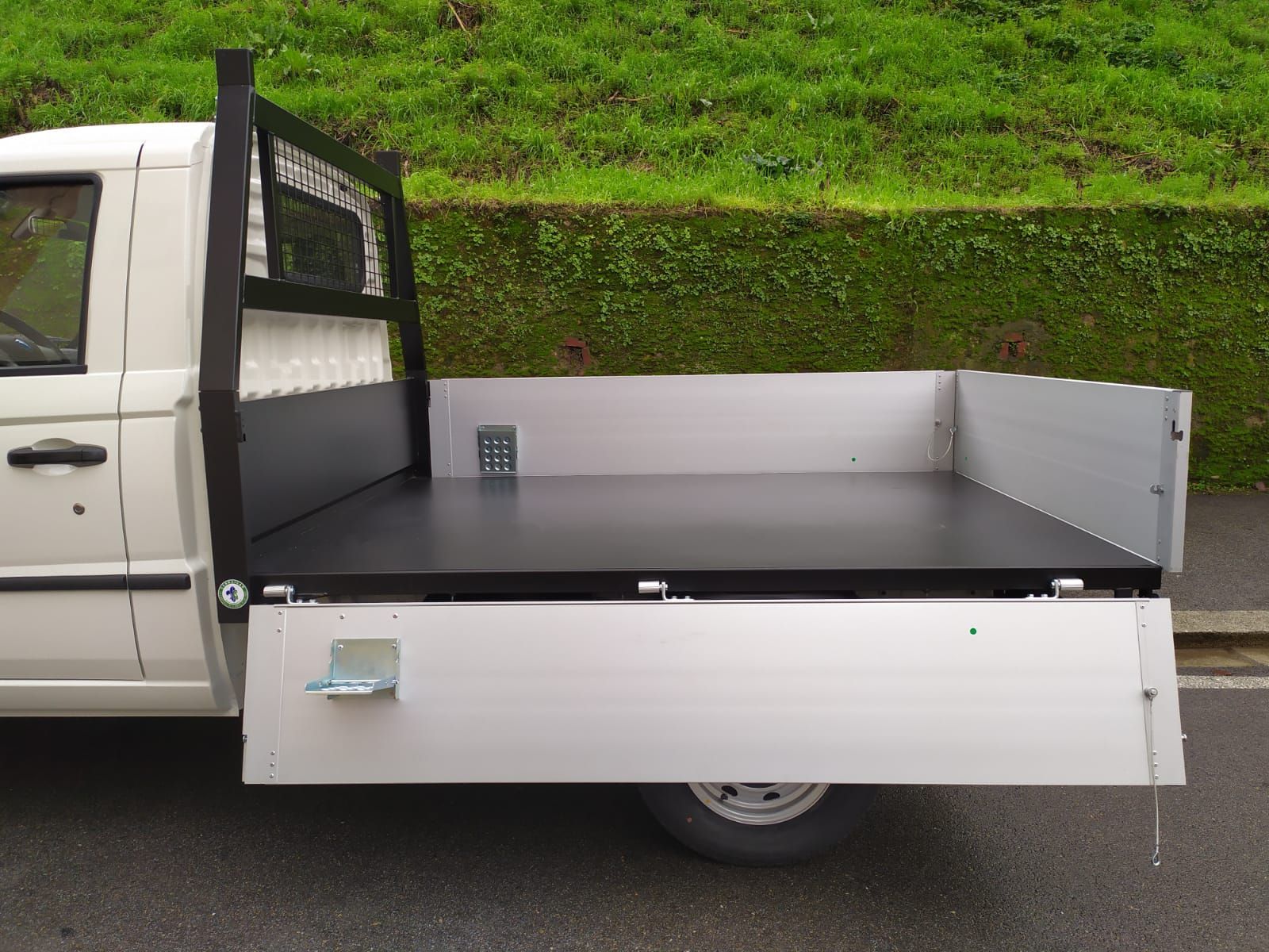 Un camion bianco con un cassone nero è parcheggiato sul ciglio della strada.