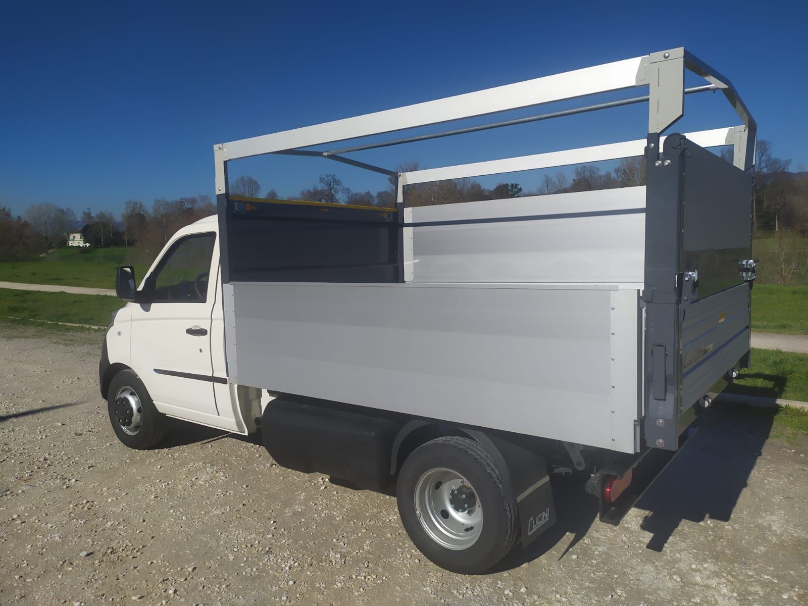 Un camion bianco con un portapacchi sul tetto è parcheggiato in uno spiazzo ghiaioso.