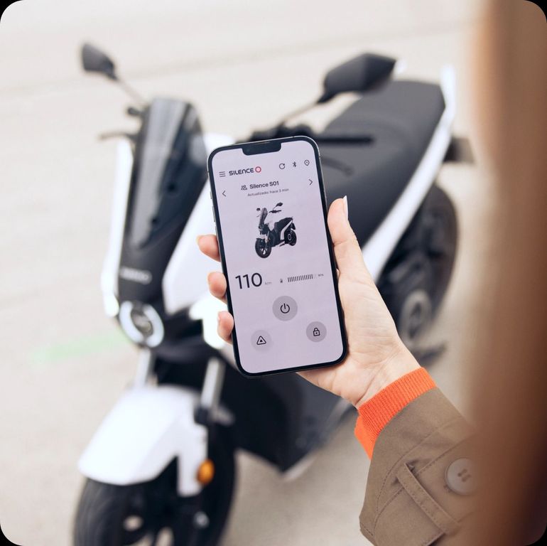 Una persona tiene in mano un telefono cellulare davanti a uno scooter.