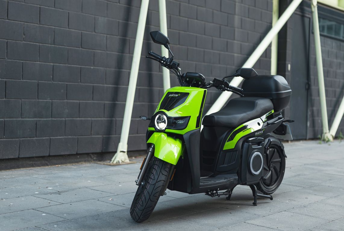 Uno scooter verde e nero è parcheggiato davanti a un muro di mattoni.