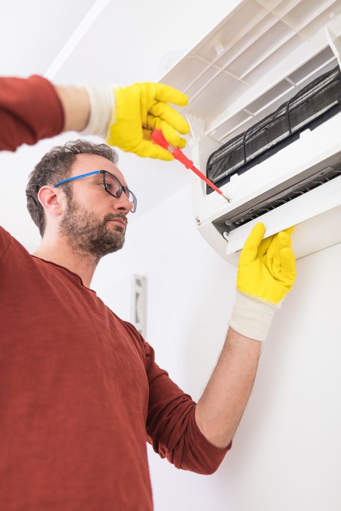 A Man is Fixing an Air Conditioner With a Screwdriver — Revive Air Conditioning in Campbelltown, NSW