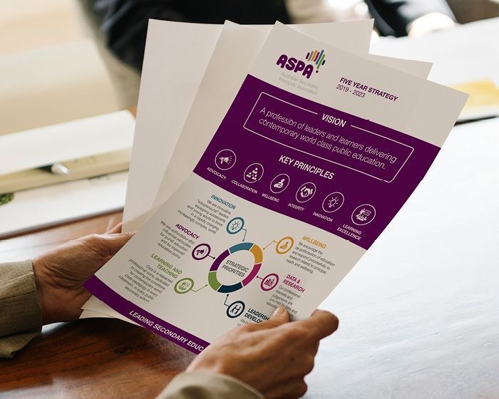 Hands holding a purple and white brochure with icons and charts on a table.