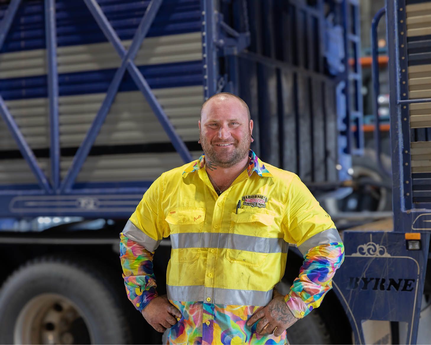 Worker in a yellow high-visibility shirt stands in front of a large truck.