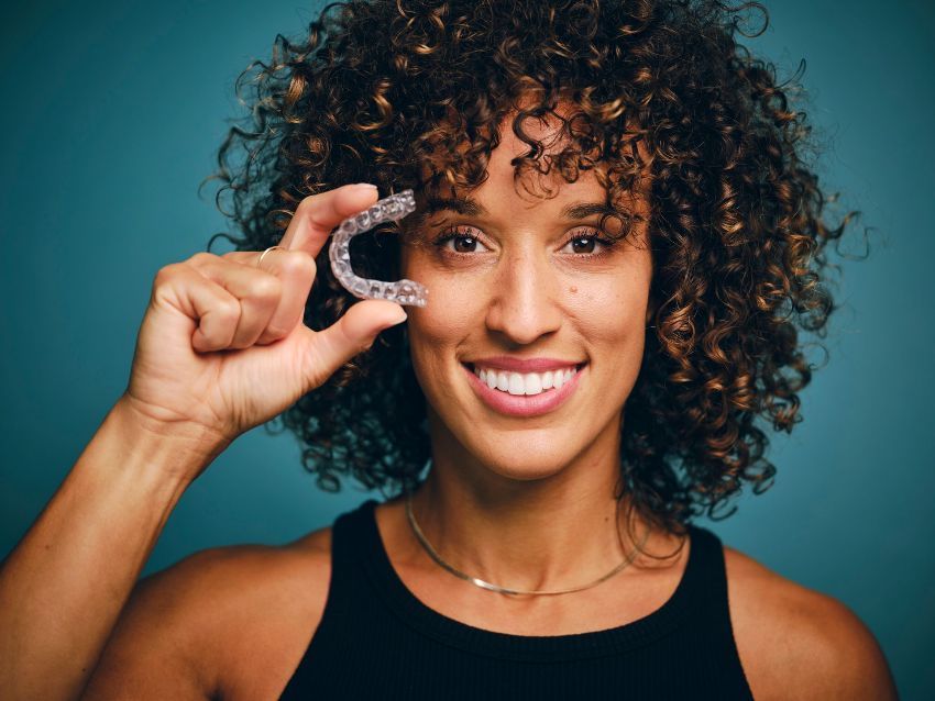 a woman with curly hair is holding a clear orthodontic aligner in her hand 