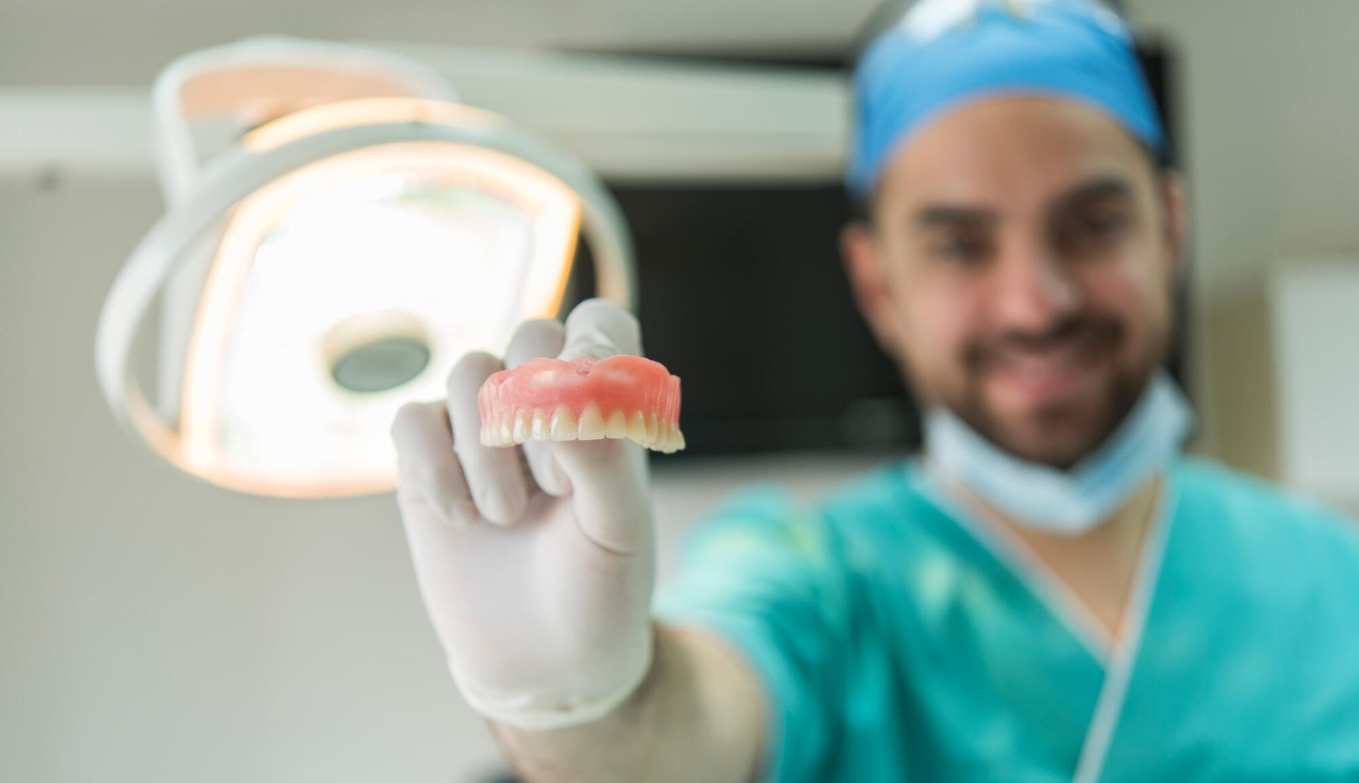 A dentist is holding a denture in his hand in an operating room.