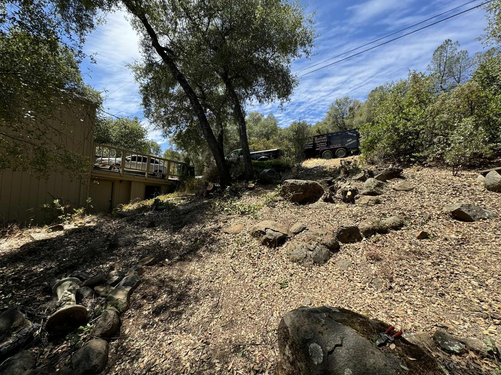 A vehicle ascending a dry, rocky hillside with scattered foliage and trees under a partly cloudy sky.