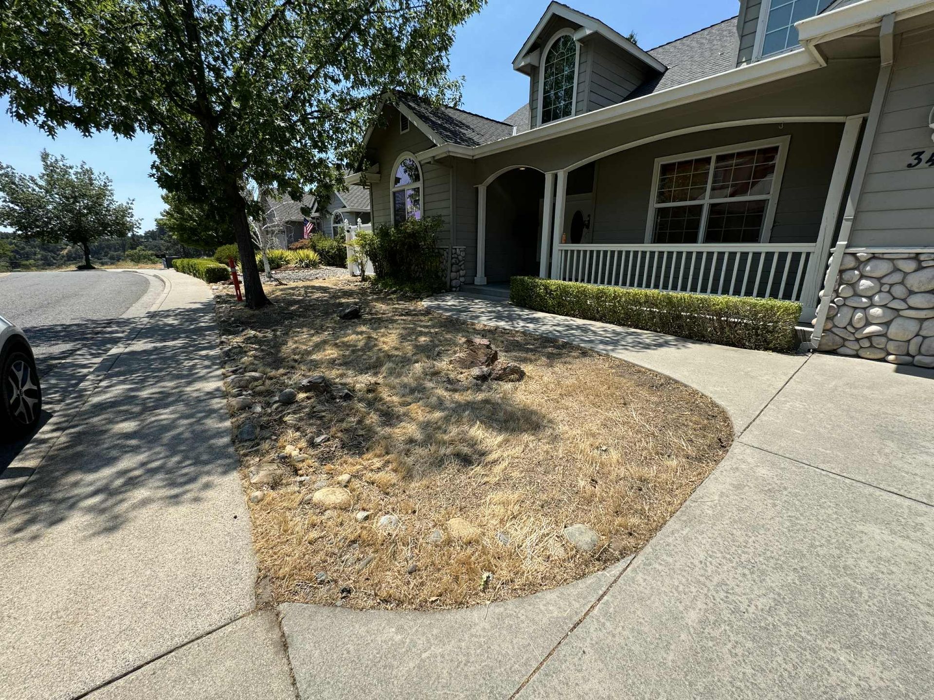 A house with a dry, brown garden bed in front, sidewalk, and street on a sunny day.