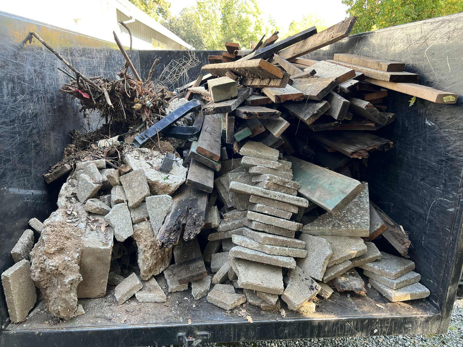 Dumpster filled with wood scraps, concrete blocks, and debris.