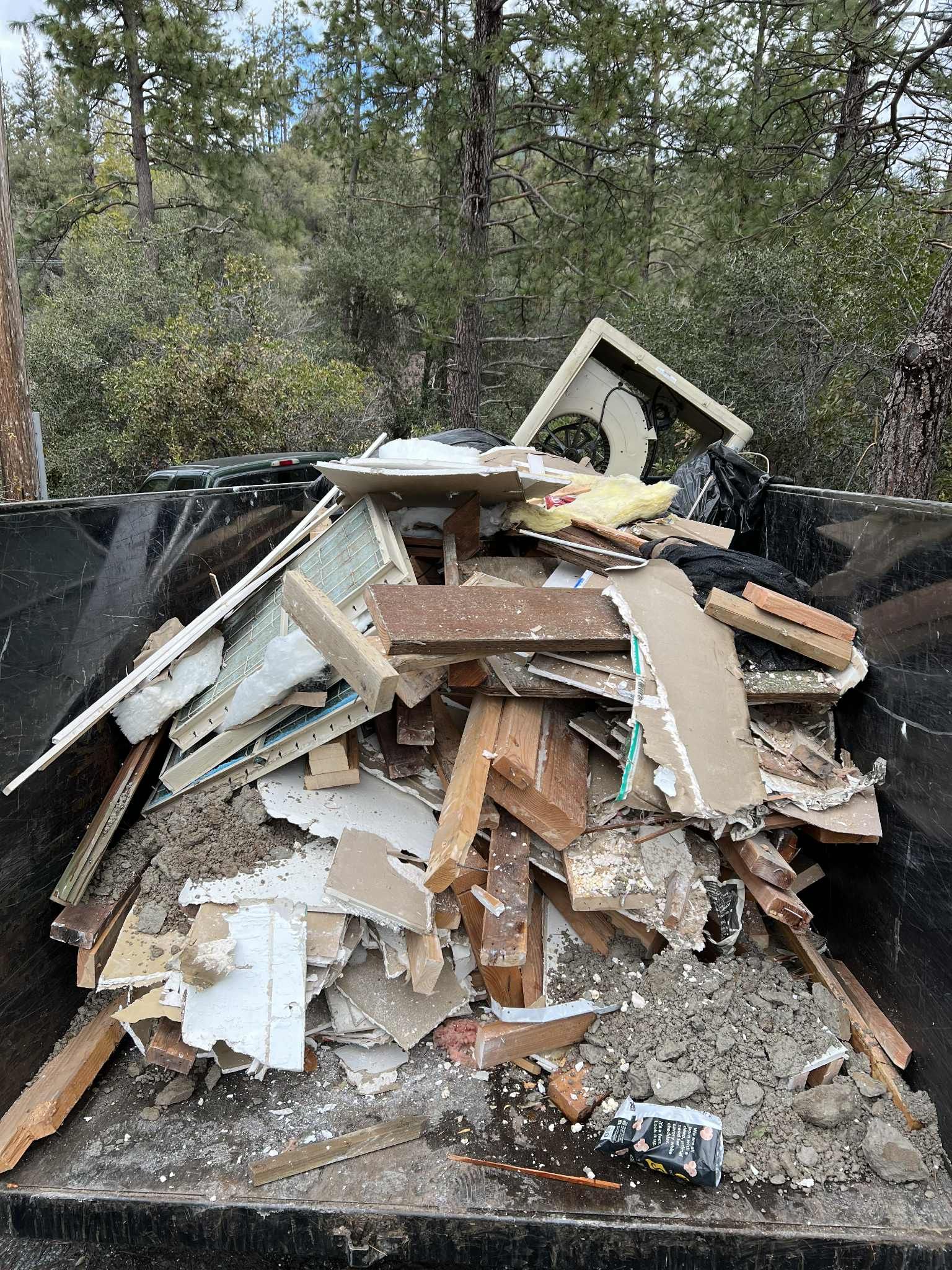 Pile of construction debris in a black dumpster; wood, drywall, and other materials.
