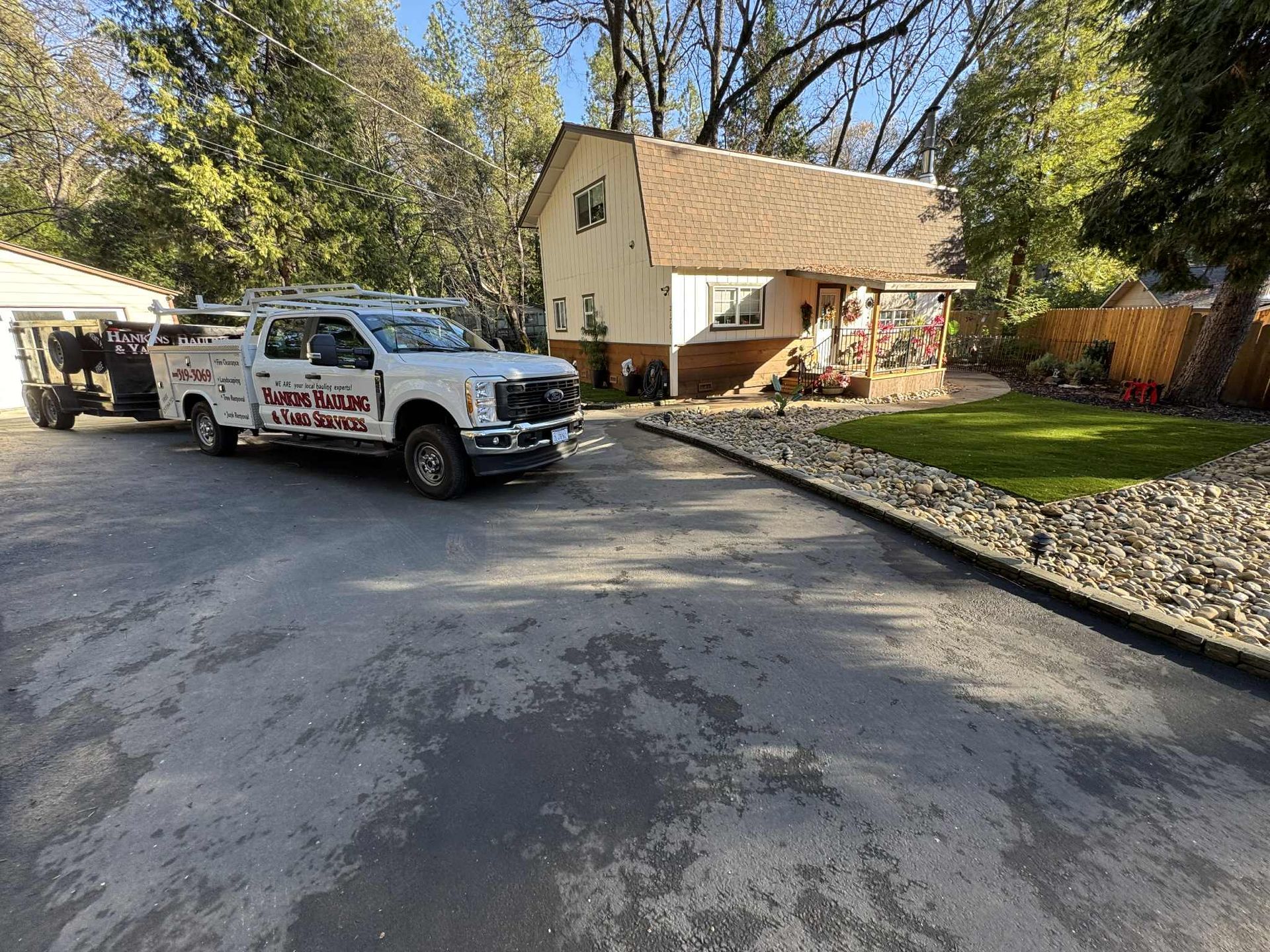 White truck with trailer parked in front of a two-story house with tan stucco and brown roof.