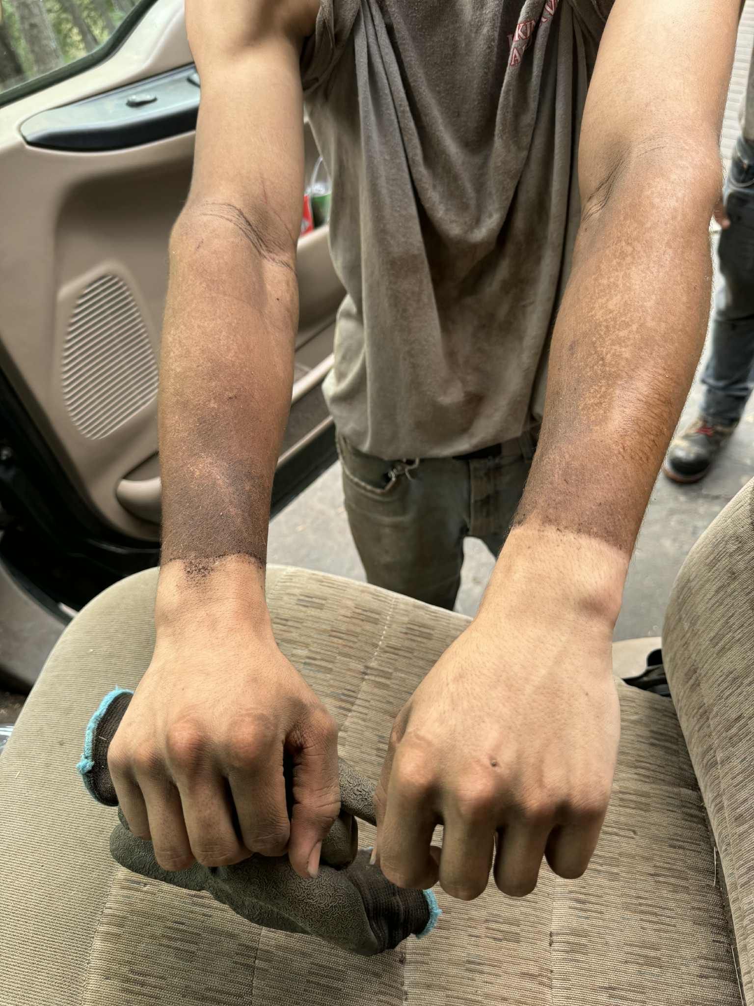 Person with dusty arms, holding a dirty tool, inside a vehicle.