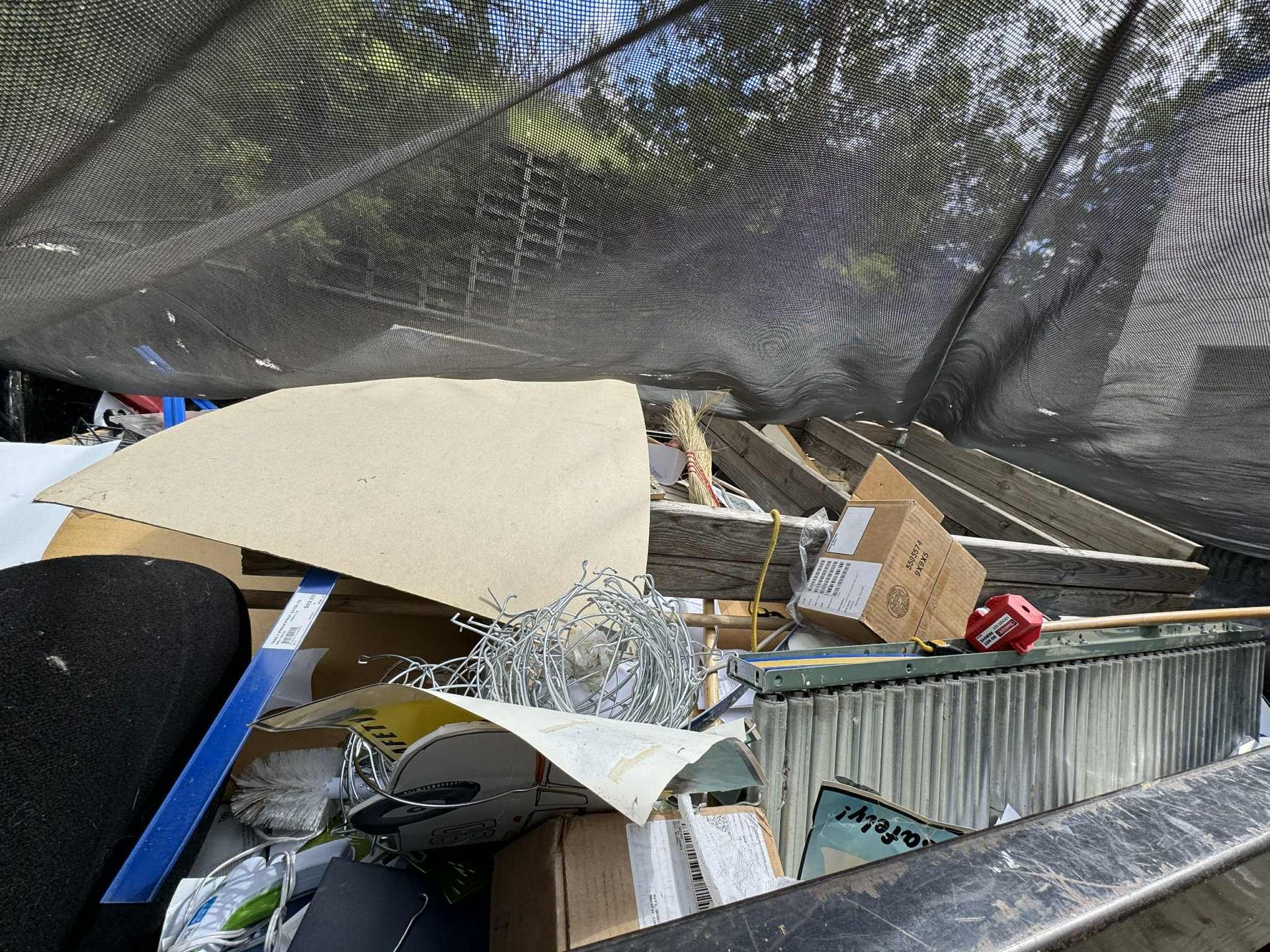 A pile of debris, including wood and cardboard, under a black mesh canopy.