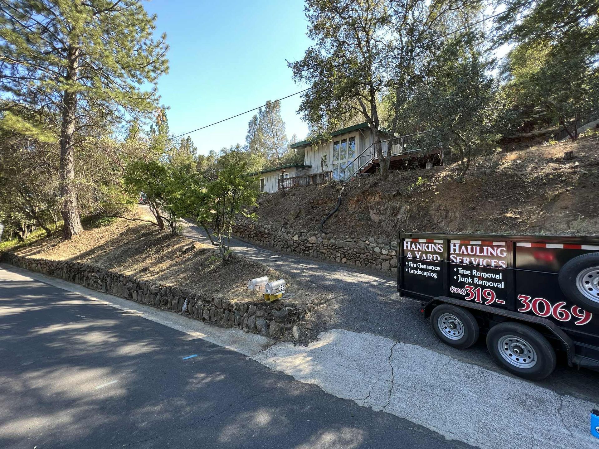Gravel driveway leading to a house on a hillside, with a hauling trailer parked on the side of the road.